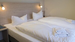Un lit double avec du linge de lit blanc et des oreillers, une table de chevet avec une lampe et une tête de lit en bois.