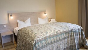 Ein ordentlich bezogenes Bett mit einem gemusterten Überwurf, einem Holzkopfstück und Nachttischlampen.