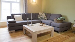 Ein Wohnzimmer mit grauem Sofa, einem Holztisch und einem Fenster mit Vorhängen.
