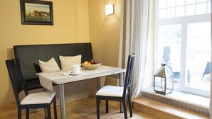 Una habitación pequeña con una cama, una mesa con sillas, un frutero y una ventana con cortinas.