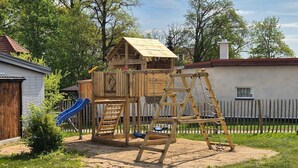 Una estructura de madera para juegos con un tobogán y una escalera de escalada en un patio trasero.
