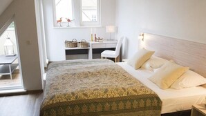 Quarto com cama grande, uma escrivaninha e uma cadeira. Há uma janela com vista para o exterior.