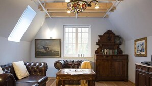A cozy room with a leather sofa, a wooden table, a bookshelf, and a large window. - Admiralssuite Wf-46 - Der Westflügel (Stolpe auf Usedom)