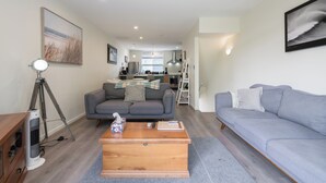 A modern living room with a grey sofa, a wooden coffee table, and a grey couch. There is a tripod and a fan in the corner. - Spacious Home Near CBD | SPA Pool | Parking | 3BR (Auckland)
