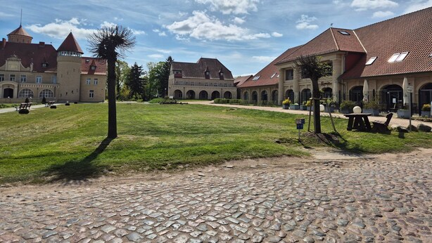 A courtyard with cobblestone paths, a grassy lawn, and historic buildings with arched walkways. - Storchennest Wf-52 - Der Westflügel (Stolpe auf Usedom)