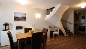 A modern kitchen with a built-in oven, a dining area with a wooden table and chairs, and a staircase with a white railing. - Storchennest Wf-52 - Der Westflügel (Stolpe auf Usedom)