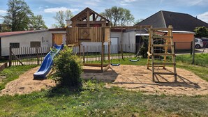 A playground with a slide and swings, surrounded by a wooden fence and a house in the background. - Storchennest Wf-52 - Der Westflügel (Stolpe auf Usedom)