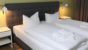 Un lit bien fait, avec du linge de lit blanc et des oreillers, une tête de lit sombre et deux lampes de chevet posées sur des tables de chevet blanches.
