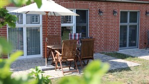 Une terrasse avec une table et des chaises, un parasol blanc et un bâtiment en briques doté de fenêtres et de portes.