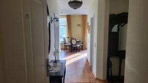 A hallway leading to a dining area with a table and chairs, a red rug, and a ceiling light fixture.