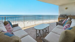 Un balcón con vistas a la playa, un conjunto de sofás, una mesa y una parrilla.