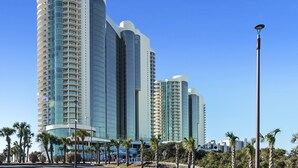 Un hotel moderno de gran altura con varios balcones, una fachada curva y palmeras en primer plano.