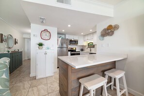 A modern kitchen with white cabinetry, a central island with stools, a microwave, and a refrigerator.