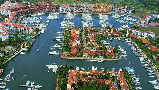 Un puerto deportivo con numerosas embarcaciones amarradas, rodeado de edificios con tejados rojos y una zona de piscina central.