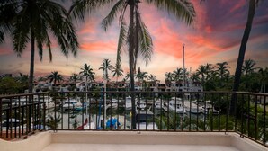 Un balcón con vista a un puerto deportivo y palmeras bajo un cielo al atardecer.