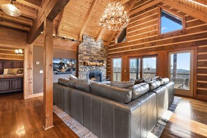 Relax in a spacious living area with a large L-shaped sofa, stone fireplace, and high ceiling with exposed beams.