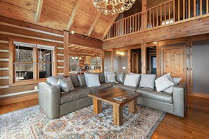 A spacious living room with a large sectional sofa, a wooden coffee table, and a patterned rug. - Stunning Cabin Overlooking the Blue Ridge Mountains (Seven Devils)