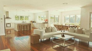 A spacious living area with a sofa, coffee table, and dining table. The room features wooden flooring, large windows, and a kitchen area with a central island. - The York Residence in Hartley NSW - Newly Listed (Hartley)