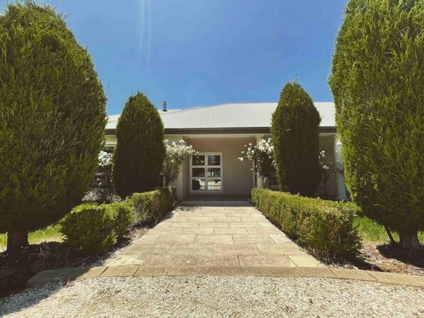 A building with a paved entrance, surrounded by neatly trimmed hedges and a gravel path.