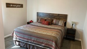 A bedroom with a wooden headboard, a patterned bedspread, and a small nightstand with a lamp. - Unique Farmhouse in quiet country setting with beautiful views (La Crosse)