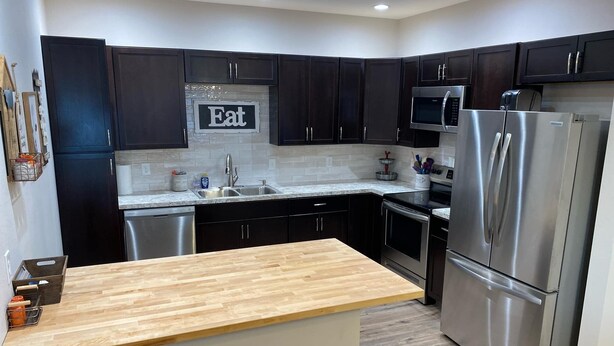A modern kitchen with dark cabinets, stainless steel appliances, a wooden countertop, and a 'Eat' sign on the wall. - Unique Farmhouse in quiet country setting with beautiful views (La Crosse)