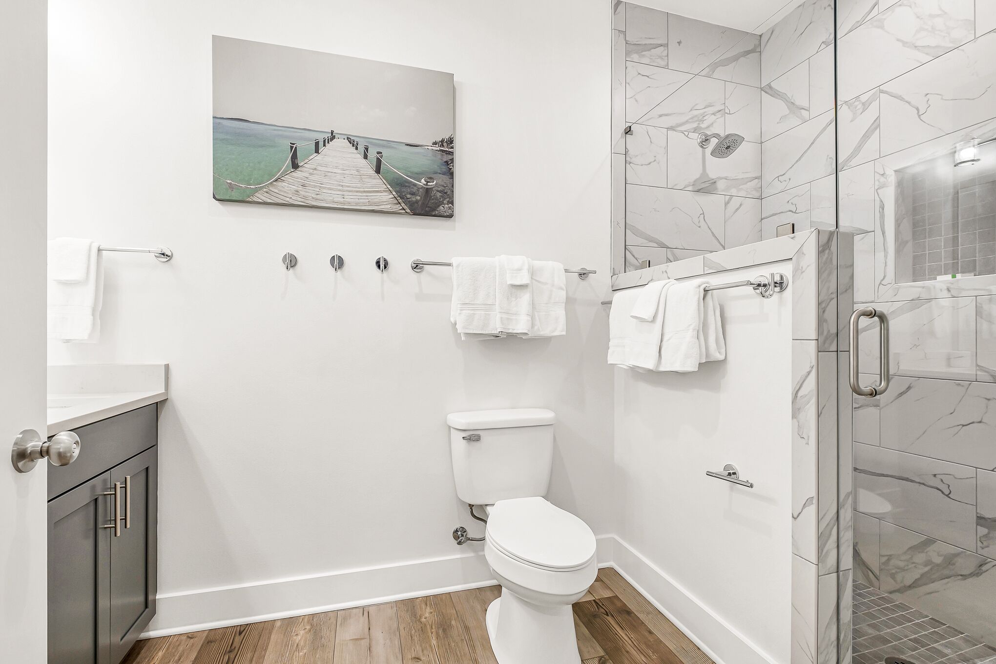 A modern bathroom with a marble shower, a toilet, and a wooden floor.