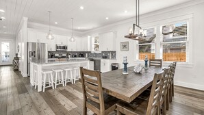 A modern kitchen with white cabinetry, a wooden dining table, and bar stools.