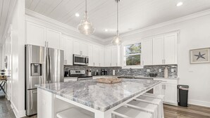 A modern kitchen with white cabinets, stainless steel appliances, a marble island, and pendant lighting.
