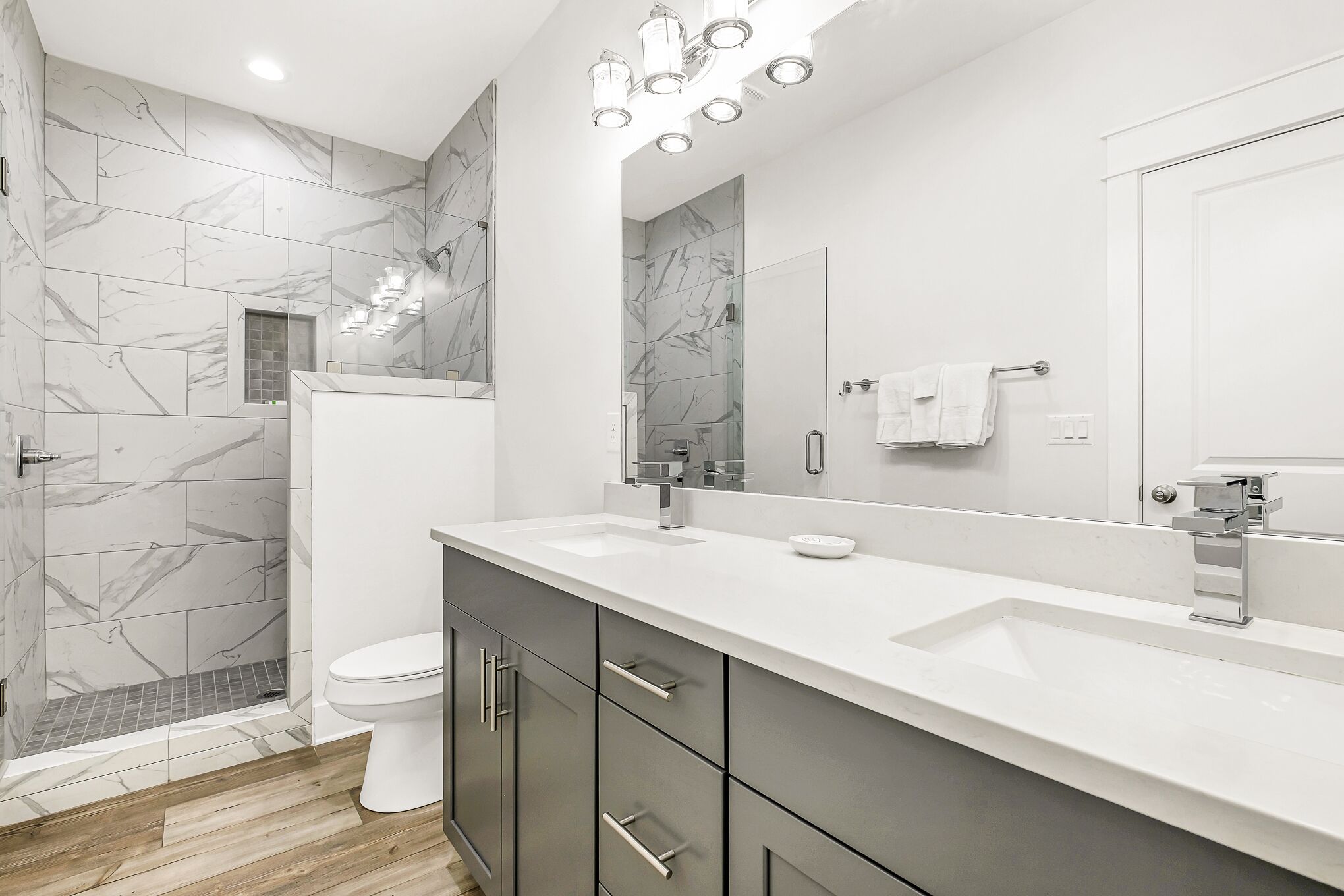 Un baño moderno con un lavabo blanco, un espejo grande y una zona de ducha con azulejos de mármol.