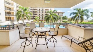 Un balcon avec une table ronde et des chaises, donnant sur une piscine et des palmiers.