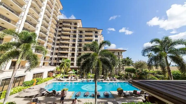 Un hôtel doté d’une piscine entourée de palmiers et de chaises longues.