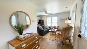 Un salon comprenant un canapé, une table basse, un fauteuil, une commode en bois, un miroir et un ventilateur de plafond.