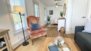 Un salon comprenant un fauteuil moelleux, une lampe sur pied, une table basse avec un livre et des objets décoratifs, un canapé foncé et une petite table d’appoint.