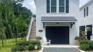 Une maison blanche à deux étages, avec un garage, une allée en gravier et un petit porche doté d’une chaise.