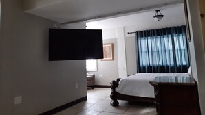 A bedroom with a bed, a television mounted on the wall, a bedside table, and a window with curtains.