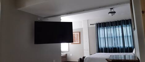 A bedroom with a bed, a television mounted on the wall, a bedside table, and a window with curtains.