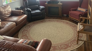 Ein Wohnzimmer mit Kamin, Ledersofas, einem Holzstuhl, einem runden Teppich und einem Deckenventilator.