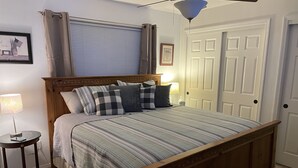 Ein Schlafzimmer mit einem hölzernen Bett, einem Nachttisch mit Lampe, einem Fenster mit Jalousien und einer Tür.
