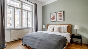Ein Schlafzimmer mit einem großen Bett, zwei Nachttischlampen, einer Heizung und einem Fenster mit Vorhängen.