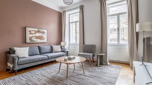 Ein modernes Wohnzimmer mit grauem Sofa, einem kleinen runden Tisch, einem grauen Sessel und einem großen Fenster mit Vorhängen.