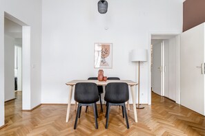 A dining area with a wooden table, two black chairs, a vase, and a framed picture on the wall.