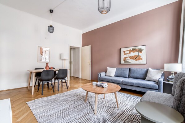 A modern living room with a grey sofa, a coffee table, and a dining area with chairs and a table.