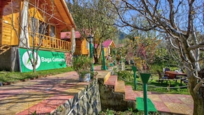 A wooden lodge with a green sign, outdoor seating, and a stone wall. - Attic Cottage by Dumnu Homes (Manali)