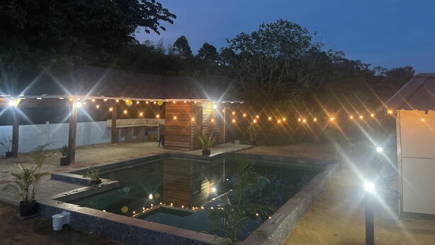 Ein Poolbereich mit Holzterrasse, Lichterketten und einem kleinen Gebäude.