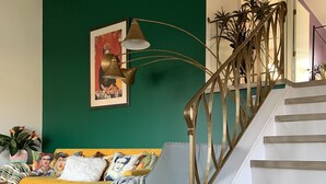 A living room with a green accent wall, a yellow sofa, a patterned rug, and a staircase with a metal railing. - Pet Friendly, Near O’Hare, Fenced in, Cheerful Frida & Diego Home, up to 6 ppl (Wood Dale)
