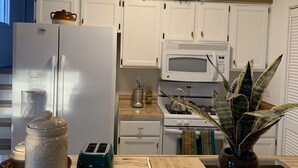 A kitchen with white cabinets, a microwave, a stove, and a refrigerator. There are two green placemats on the counter. - Pet Friendly, Near O’Hare, Fenced in, Cheerful Frida & Diego Home, up to 6 ppl (Wood Dale)