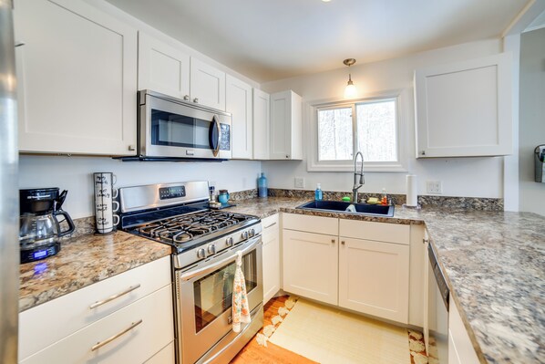 A modern kitchen with white cabinets, a stainless steel stove, a microwave, and a granite countertop. - Manistique Lake Retreat w/ Dock! (Germfask)