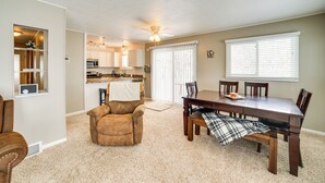A spacious living area with a dining table, chairs, a brown leather chair, a kitchen in the background, and a ceiling fan. - Manistique Lake Retreat w/ Dock! (Germfask)