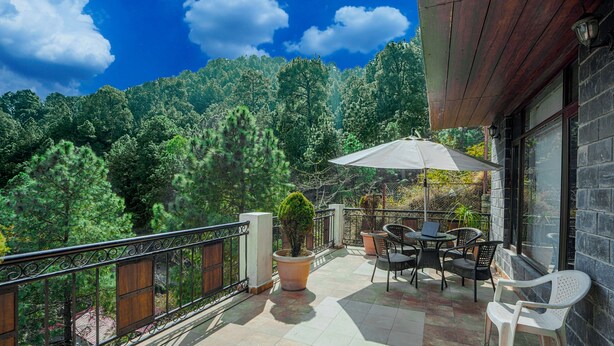 A balcony with outdoor furniture, a potted plant, and a view of a forested hillside. - Alayam 3 BHK by Dumnu Homes (Krishangarh)