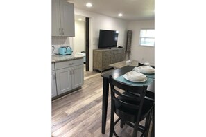 Modern kitchen with flat-screen TV, toaster, and dining area with a wooden table for two.